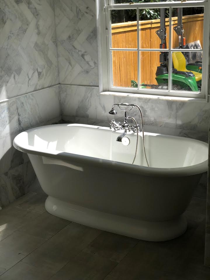 Freestanding pedestal tub with chrome telephone-style faucet in a marble tiled bathroom