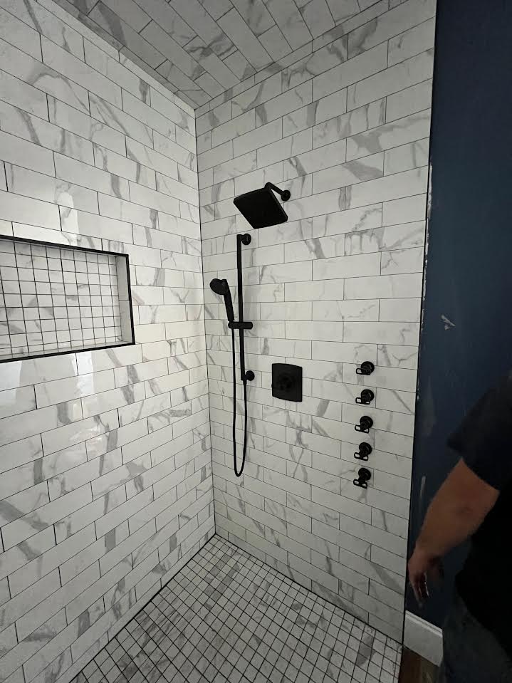 Custom tile shower with matte black rain head, hand shower and body sprays plumbed by Big Branch Plumbing