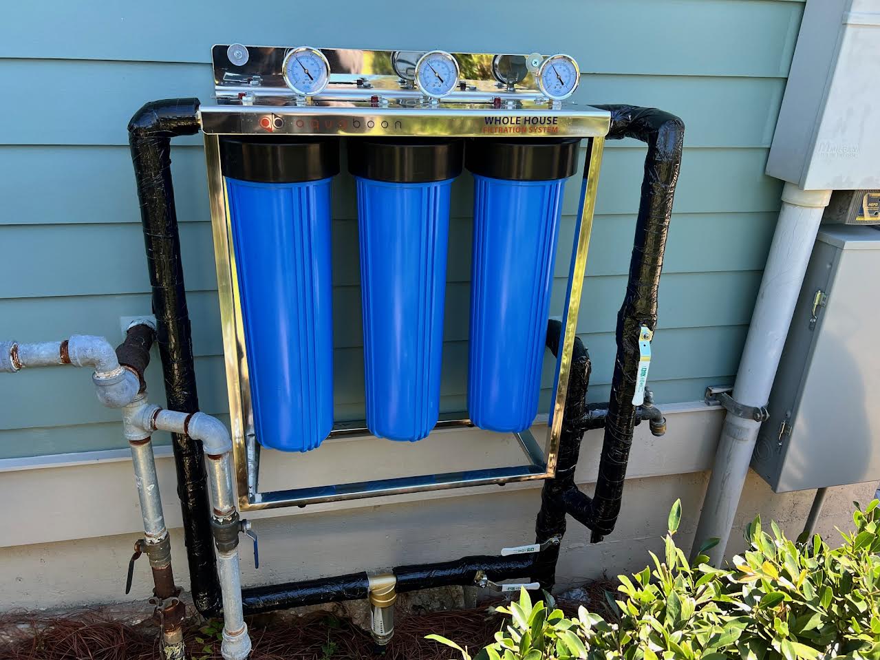 Aquaboon whole-house water filtration system installed on the exterior water service line of a Louisiana home